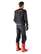 Alpinestars Missile V3 Ignition Lederjacke, Rennsport-Motorradjacke, Schwarz und Rot Fluo, Rückansicht eines Fahrers in vollständiger Rennbekleidung mit passender Lederhose, Handschuhen und roten Stiefeln, mit sportlichem Aero-Höcker und markantem Branding am unteren Rücken.