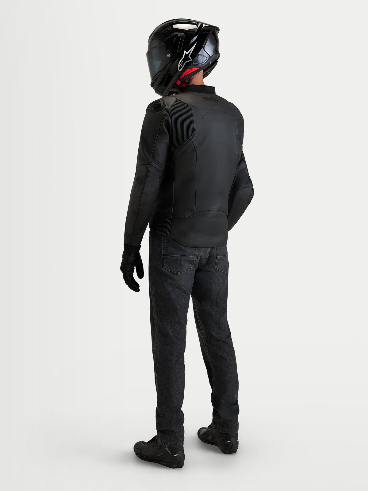 Alpinestars Caliber V2 Leather Jacket, Black men's sport leather motorcycle jacket, rear view of a rider wearing full gear with helmet and black denim jeans