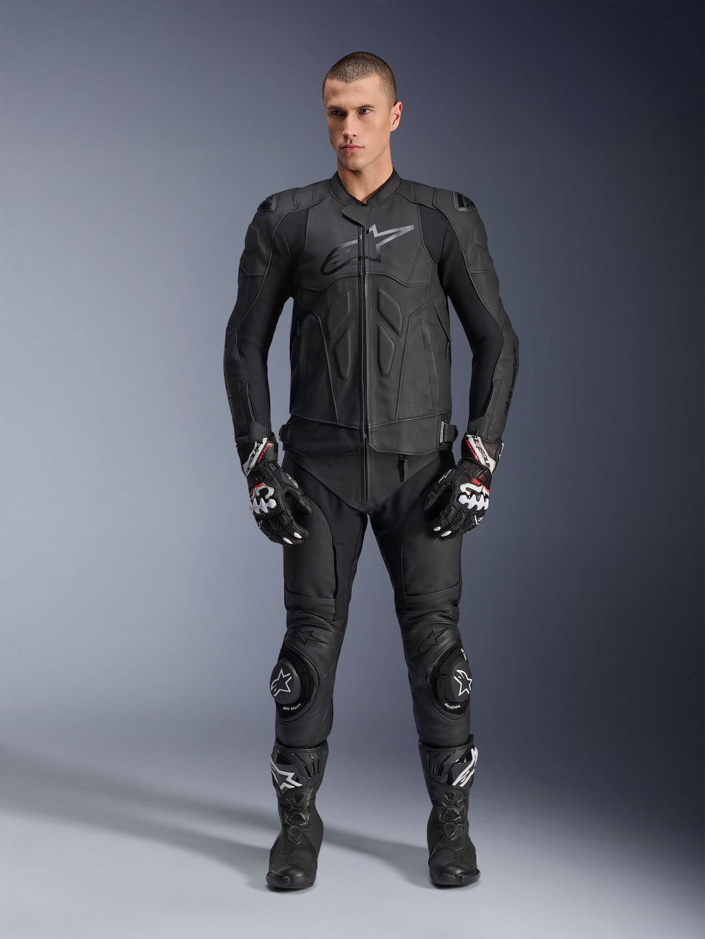 Alpinestars Dusk Leather Jacket, Black, worn by a male model as part of a complete racing-inspired outfit including matching leather pants, gloves, and boots, sleek ergonomic design with armored shoulders and chest branding.