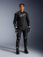 Male model wearing the Alpinestars Dusk Leather Jacket in Black and White, featuring prominent white logos on the chest and shoulders, paired with matching black leather motorcycle pants, black and white gloves, and black boots, complete sport racing outfit for road use.