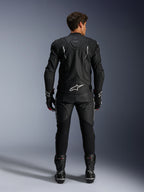 Motorradfahrer in der Rückansicht mit der Alpinestars Dusk Lederjacke und der Missile V3 Lederhose, kompletter schwarzer Lederanzug mit weißen Akzenten, Jacke mit „Dusk“-Branding und Alpinestars-Logo auf dem Rücken, kombiniert mit schwarzen Rennstiefeln und Handschuhen, abgestimmtes Motorsport-Outfit für den Straßenrennsport.