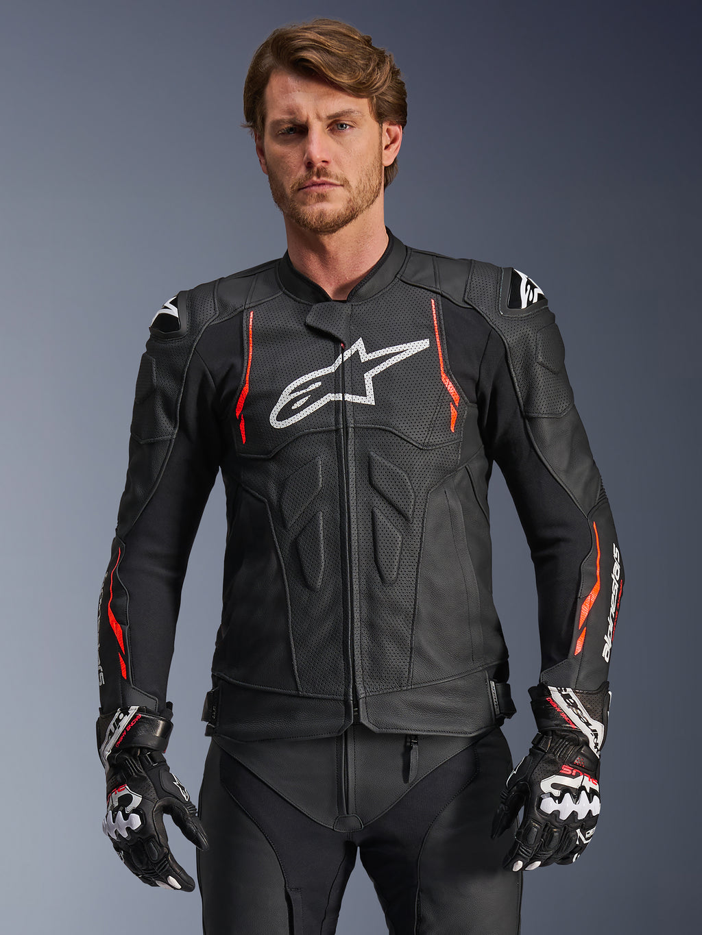Alpinestars Dusk Airflow Leather Jacket, Black with Red Fluo and White accents, Leather Motorcycle Racing Jacket, featuring extensive perforations for ventilation, white chest logo, and external shoulder sliders, worn by a model with matching racing gloves