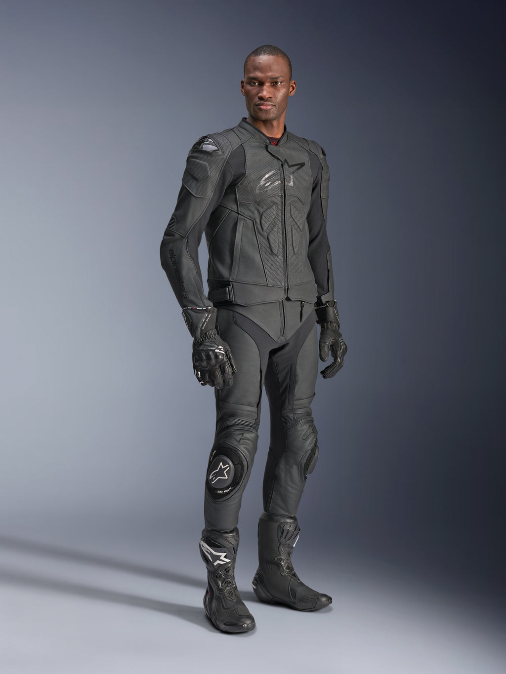 Alpinestars Dusk Airflow Lederjacke, Schwarz, getragen von einem Fahrer in kompletter technischer Ausrüstung inklusive passender Lederhose, Handschuhen und Stiefeln, mit perforierten Ledereinsätzen zur Belüftung und integrierten Protektoren für das sportliche Motorradfahren.