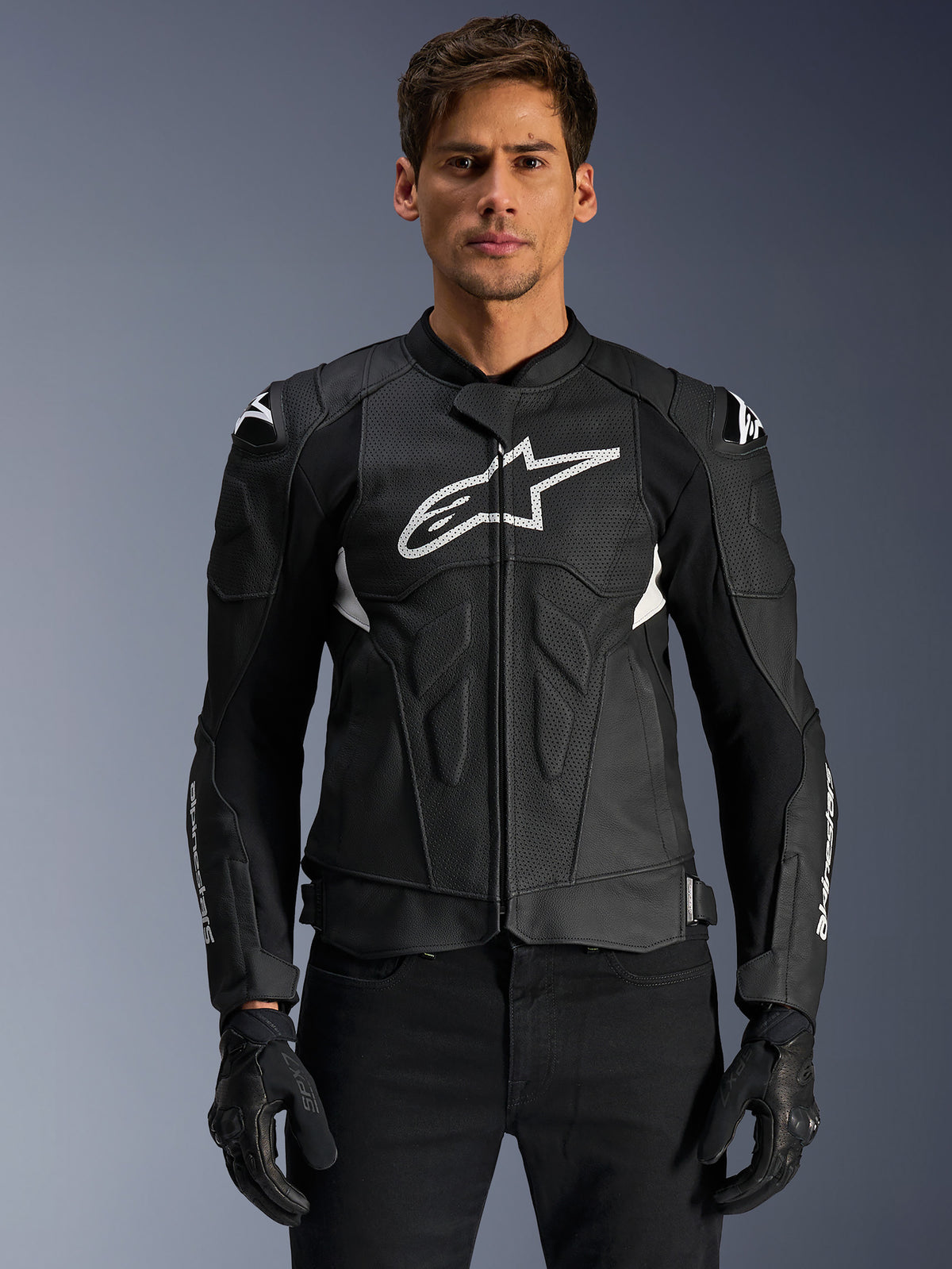 Alpinestars Dusk Airflow Lederjacke, Schwarz und Weiß, von einem Model getragen, mit perforierten Lederbahnen für Belüftung, einem großen weißen Logo auf der Brust und externen Schulterschleifern.
