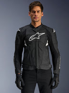 Alpinestars Dusk Airflow Lederjacke, Schwarz und Weiß, von einem Model getragen, mit perforierten Lederbahnen für Belüftung, einem großen weißen Logo auf der Brust und externen Schulterschleifern.