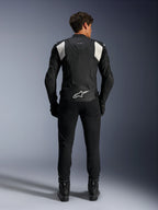 Alpinestars Dusk Airflow Lederjacke, Schwarz und Weiß, Rückansicht eines Fahrers mit schwarzer Hose und Stiefeln, mit perforiertem Leder für Belüftung, weißen Akkordeon-Stretcheinsätzen an den Schultern und weißem Branding am unteren Rücken