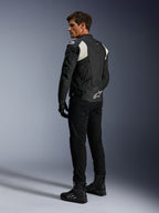 Alpinestars Dusk Airflow Lederjacke, Schwarz und Weiß, Rückansicht eines Models in der perforierten Lederjacke mit passender schwarzer Hose und Stiefeln, mit weißen Akkordeon-Stretcheinsätzen und markantem Logo am unteren Rücken, Sport-Motorradbekleidung