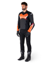 Männlicher Fahrer in der Alpinestars Faster V3 Lederjacke in Schwarz und Rot Fluo, kombiniert mit schwarzer Motorradhose, Handschuhen und Stiefeln. Die Jacke zeichnet sich durch eine vom Rennsport abgeleitete Silhouette mit markanten fluoreszierenden roten Akzenten an Brust und Ärmeln, weißem Alpinestars-Branding und einer hochwertigen Lederkonstruktion aus.