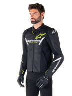 Alpinestars Faster V3 Airflow Lederjacke, Sport-Motorradjacke, Schwarz, Weiß und Gelb Fluo, getragen von einem Mann, mit perforiertem Leder für Belüftung, Alpinestars-Logos auf Brust und Ärmeln, kombiniert mit schwarzen Handschuhen.