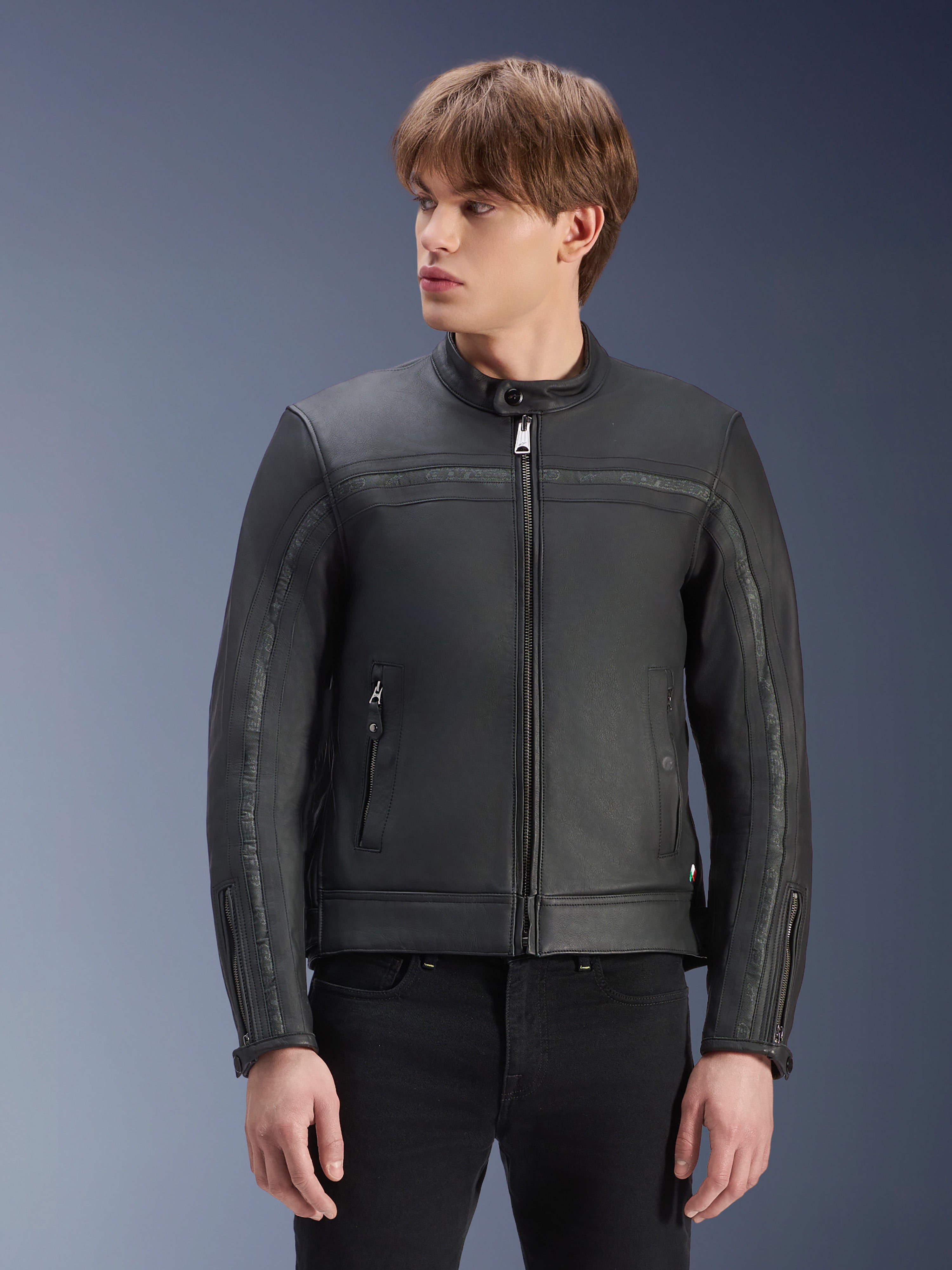 Alpinestars Dyno Lederjacke, Schwarz, Premium-Motorradjacke aus Rindsleder, getragen von einem Model mit schwarzer Hose, Heritage-inspiriertes Design mit zentralem Reißverschluss und flachem Stehkragen, urbane moderne Motorradbekleidung.
