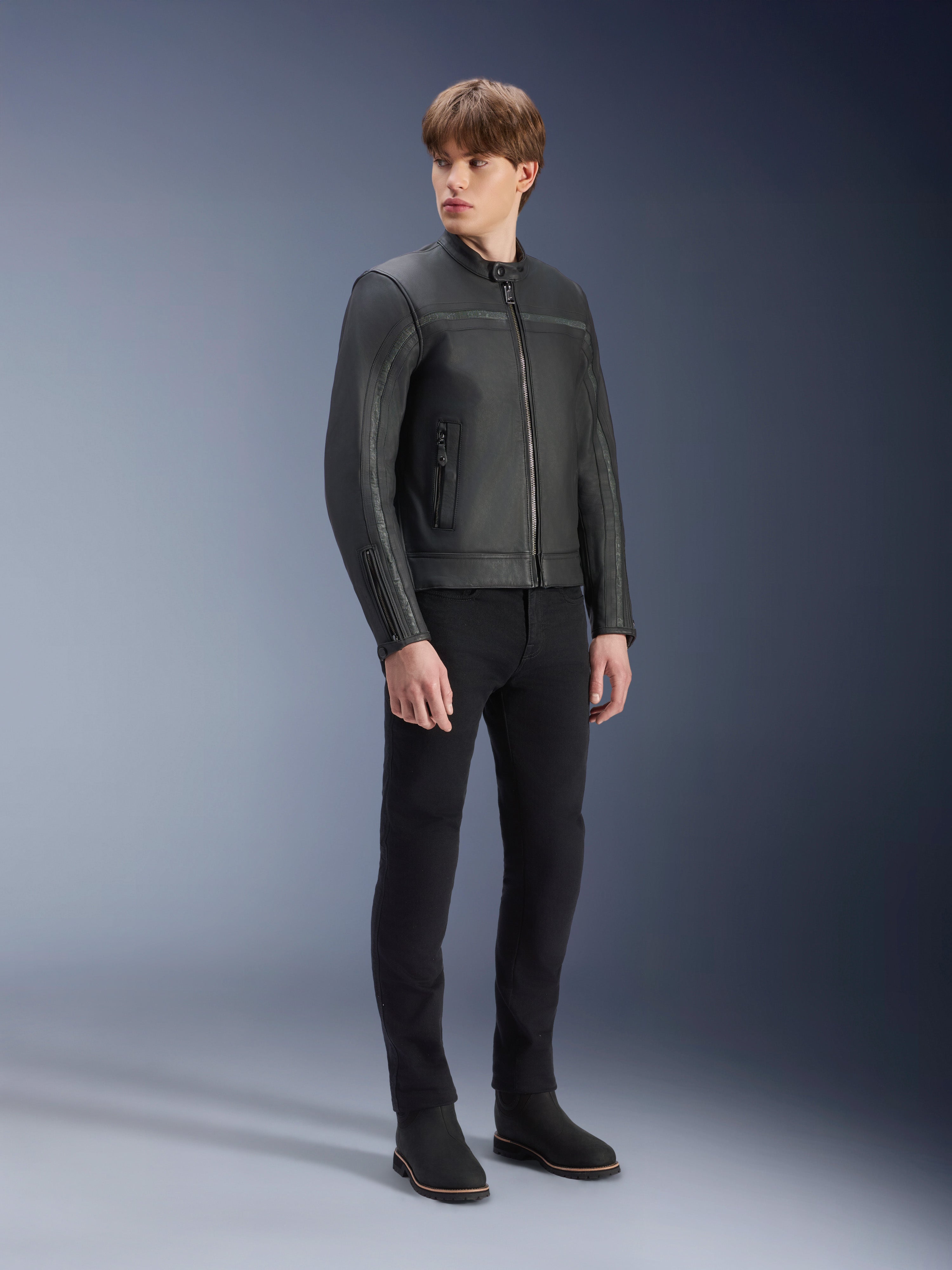 Alpinestars Dyno Lederjacke in Schwarz, hochwertige Motorradjacke aus Rindsleder, getragen von einem männlichen Model mit schwarzer Slim-Fit-Hose und schwarzen Stiefeln, Heritage-inspiriertes minimalistisches Design für urbanes zeitgenössisches Fahren, Studio-Aufnahme.