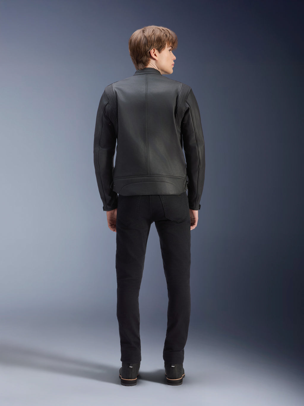Alpinestars Dyno Lederjacke, Schwarz, Rückansicht am Modell, hochwertiges Rindsleder mit Akkordeon-Schulterpaneelen, Heritage-inspirierte Motorradjacke, getragen mit schwarzer Hose und Stiefeln, urbaner zeitgenössischer Stil