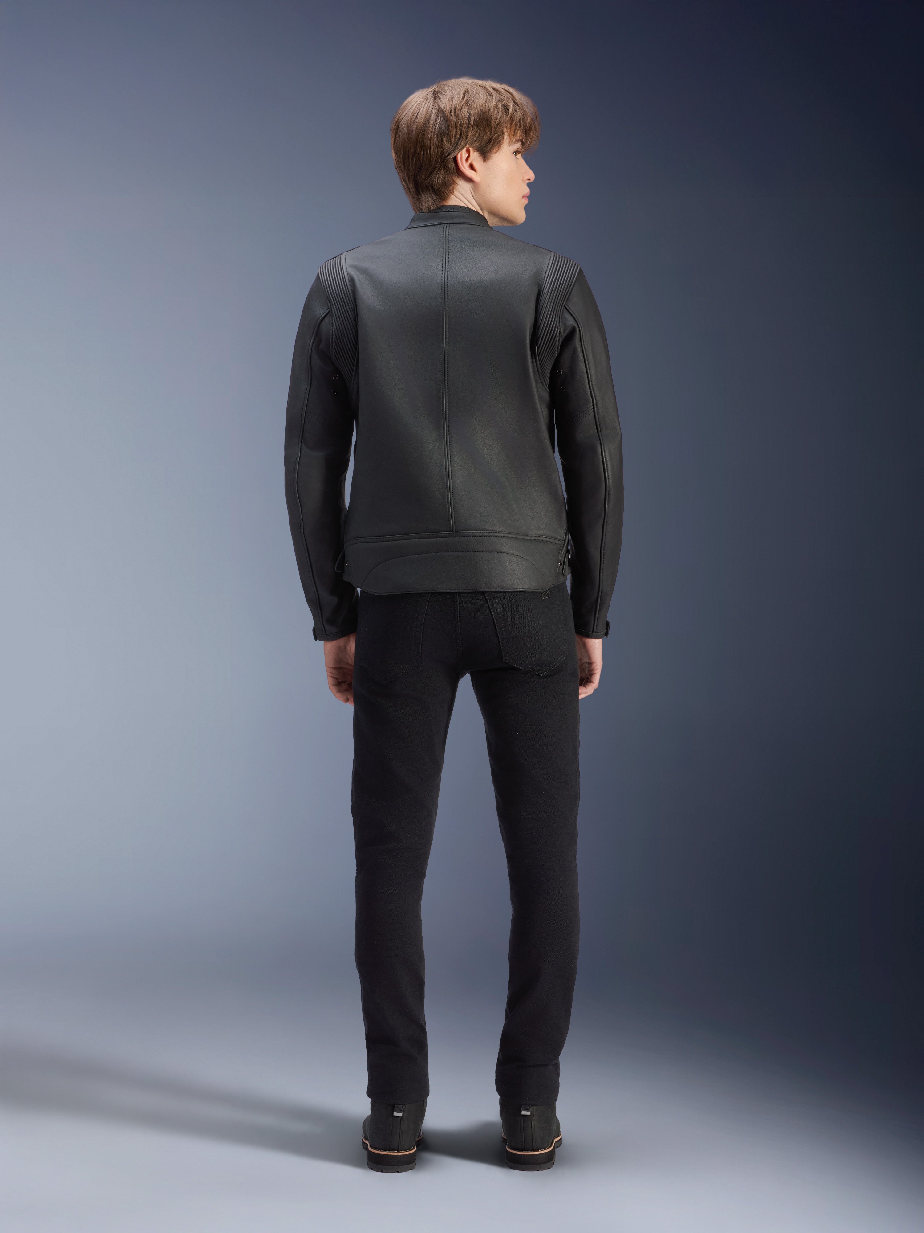Alpinestars Dyno Lederjacke, Schwarz, Rückansicht am Modell, hochwertiges Rindsleder mit Akkordeon-Schulterpaneelen, Heritage-inspirierte Motorradjacke, getragen mit schwarzer Hose und Stiefeln, urbaner zeitgenössischer Stil