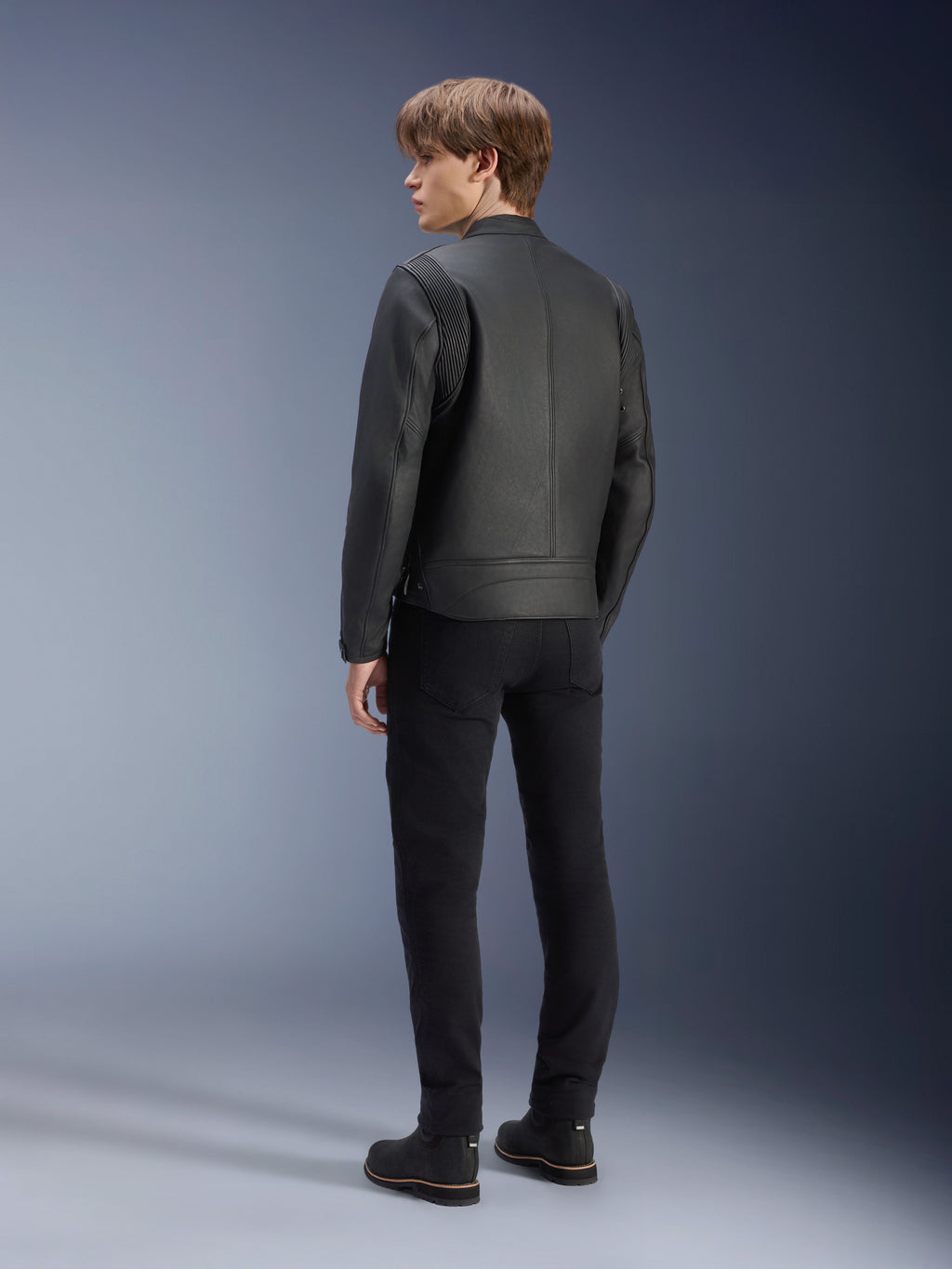Alpinestars Dyno Lederjacke, Schwarz, Rückansicht an einem männlichen Model, mit gerippten Schultereinsätzen, kombiniert mit schwarzer Hose und Stiefeln, Heritage-inspirierter urbaner Motorradstil