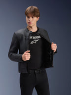 Alpinestars Dyno Lederjacke, Schwarz, getragen von einem männlichen Model über einem schwarzen T-Shirt mit Logo, hochwertige Motorradjacke aus Rindsleder, Heritage-inspiriertes Design mit dezenten Bruststreifen und zeitgemäßer urbaner Passform