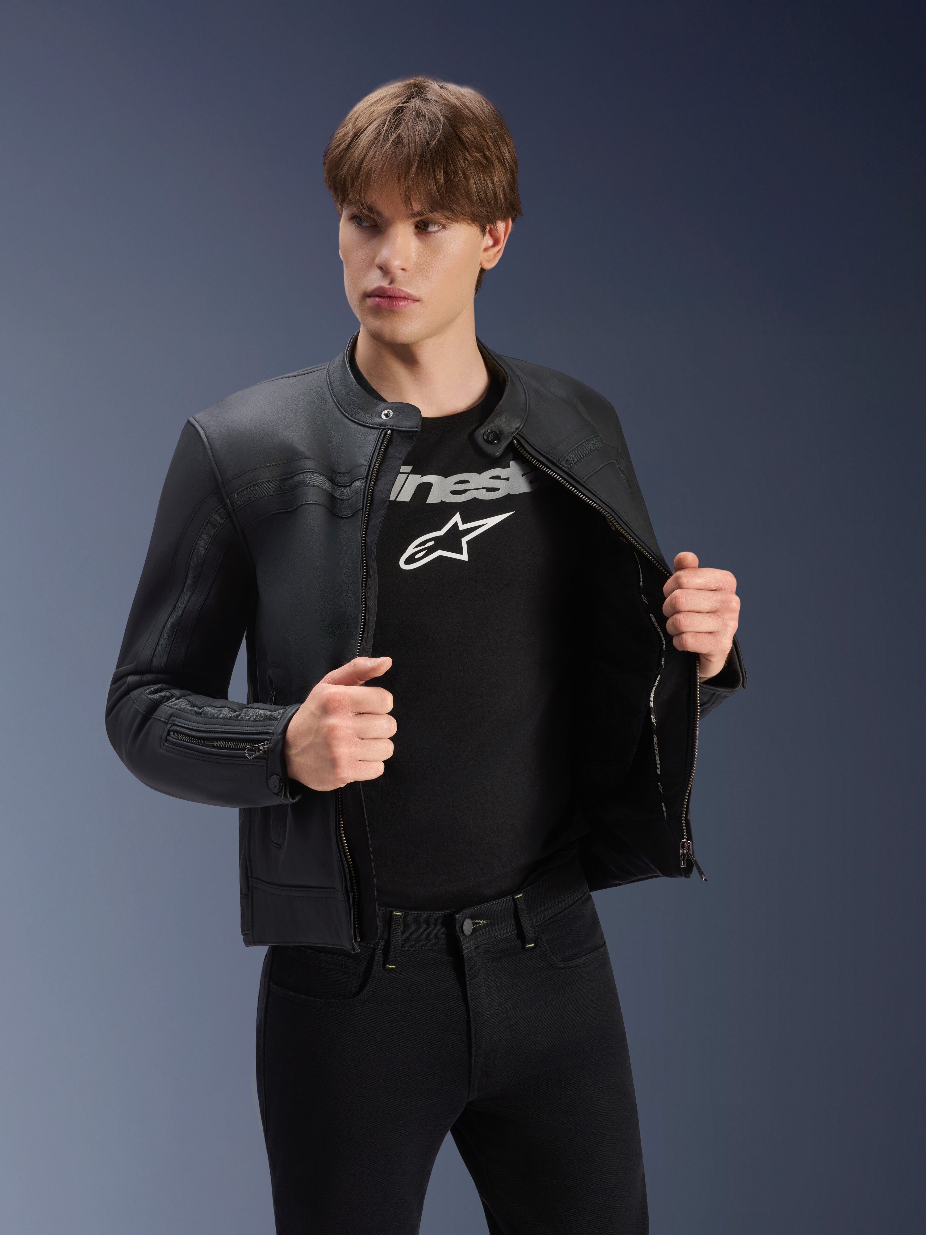 Alpinestars Dyno Lederjacke, Schwarz, getragen von einem männlichen Model über einem schwarzen T-Shirt mit Logo, hochwertige Motorradjacke aus Rindsleder, Heritage-inspiriertes Design mit dezenten Bruststreifen und zeitgemäßer urbaner Passform