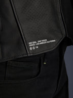 Close-up of the Alpinestars Atem V5 Leather Jacket in Black, featuring the lower back panel with 'ONE GOAL. ONE VISION. VENICE / LOS ANGELES CALIFORNIA' branding and perforated leather texture.