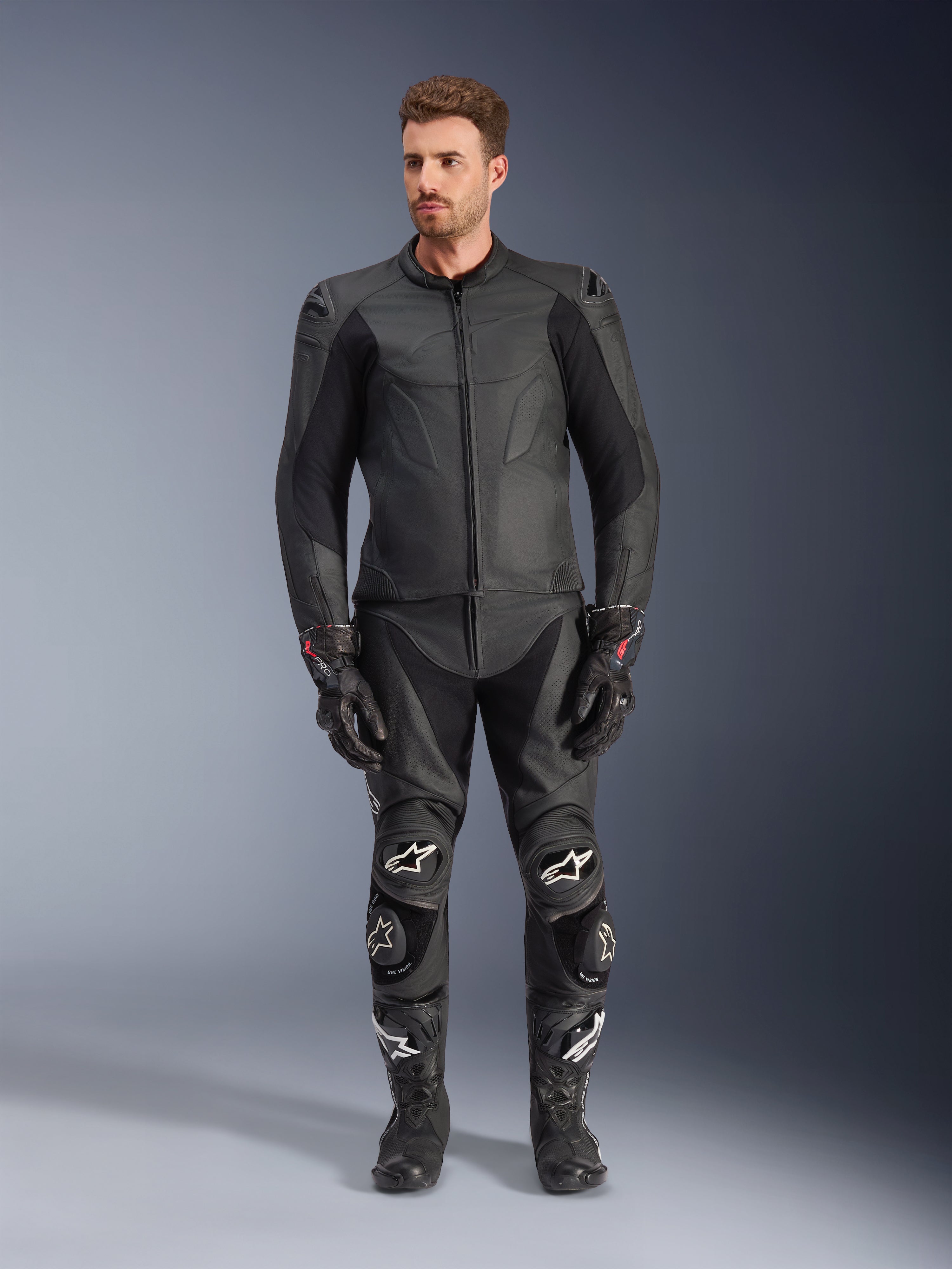 Alpinestars Caliber Lederjacke, schwarze Motorradjacke, getragen mit passender Rennsport-Hose, Handschuhen und Stiefeln, elegantes Design mit farblich abgestimmten Logos, Stretcheinsätzen an den Ärmeln und schützenden Schulter-Slidern, professionelle Studioaufnahme