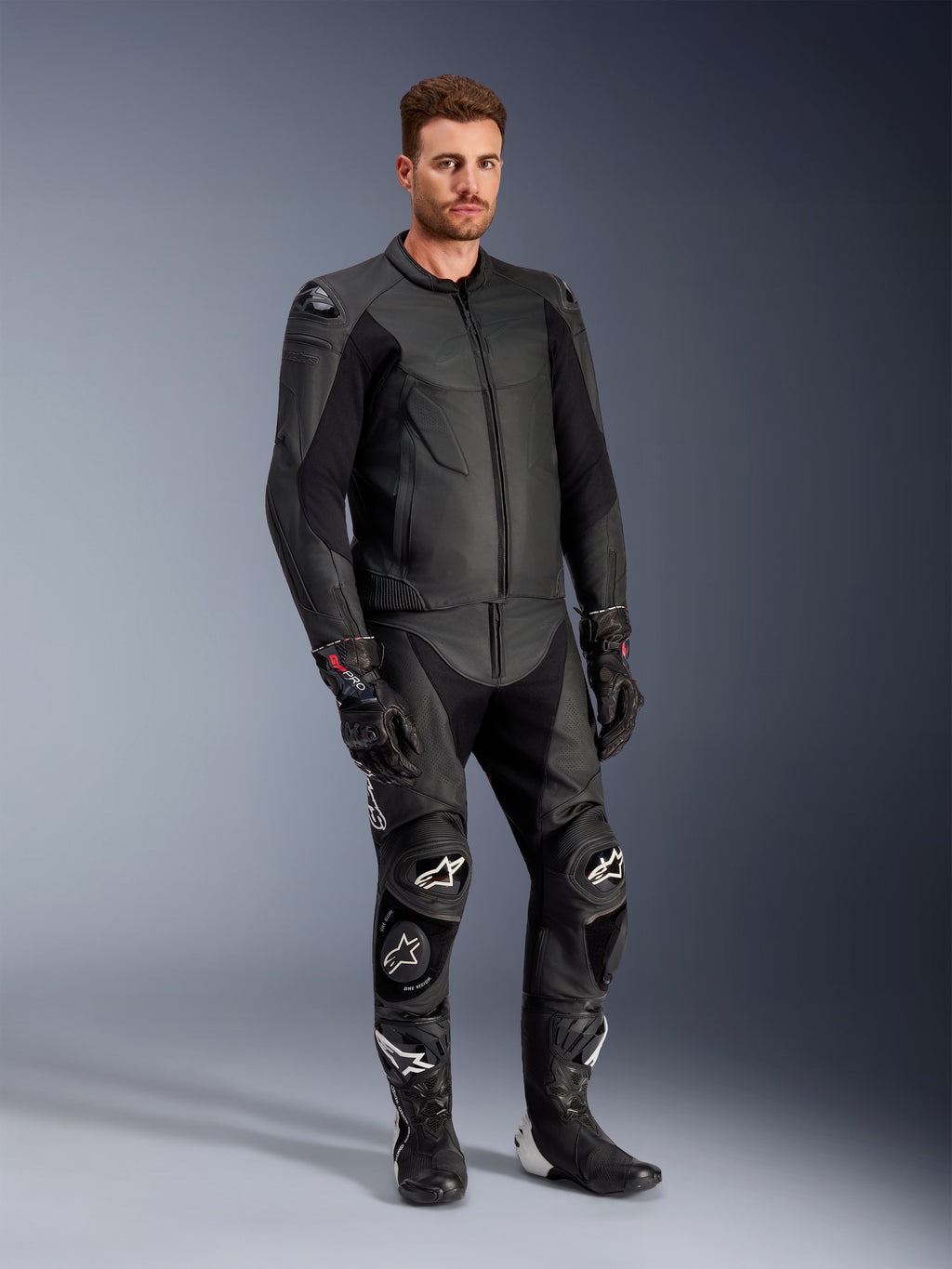 Männliches Modell in der Alpinestars Caliber Lederjacke in Schwarz, kombiniert mit passender schwarzer Leder-Motorradhose, Rennhandschuhen und Stiefeln, präsentiert ein komplettes Sport-Road-Outfit.