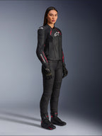 Alpinestars Stella Dusk Damen-Lederjacke, Schwarz, Diva-Pink und Weiß, getragen von einem weiblichen Model mit schwarzer Motorradhose und Stiefeln, elegante Lederkonstruktion mit pinkfarbenen Details und weißem Branding