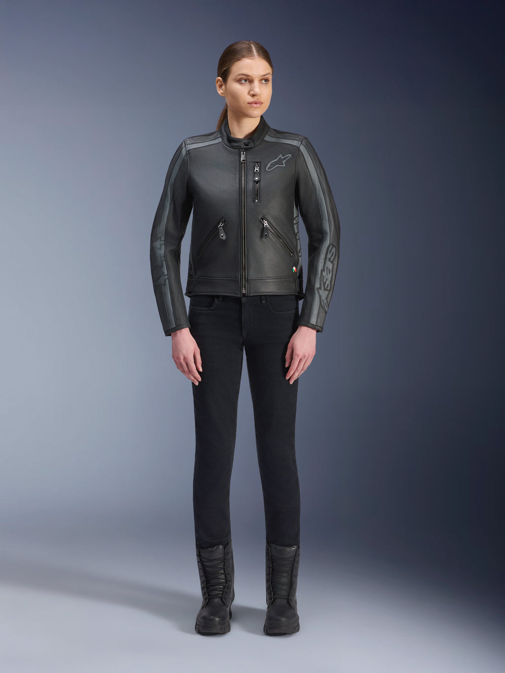 Alpinestars Stella Dyno Lederjacke, Damen-Motorradjacke, Schwarz, Tar Gray, Dunkelgrau, Ganzkörper-Studioansicht eines Models, das die Jacke mit einer schwarzen Slim-Fit-Hose und schwarzen Stiefeln trägt, gefertigt aus Rindsleder mit grauen Akzenten und dezentem Alpinestars-Branding auf der Brust und den Ärmeln.