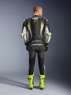 Alpinestars GP Tech V5 Einteiliger Lederkombi, Rückansicht, Schwarz, Weiß und Gelb Fluo, mit aerodynamischem Rückenhöcker mit gelbem Stern-Logo, weißes Alpinestars-Branding an Ärmeln und Rücken, passende neongelbe Rennstiefel, professionelle Motorrad-Rennausrüstung