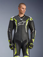 Alpinestars GP Tech V5 Einteiliger Lederkombi, Schwarz, Weiß und Gelb Fluo, professionelle Rennausrüstung, perforiertes Leder mit großem weißem Astar-Logo auf der Brust, neongelbe und weiße Akzente, getragen mit passenden Rennhandschuhen