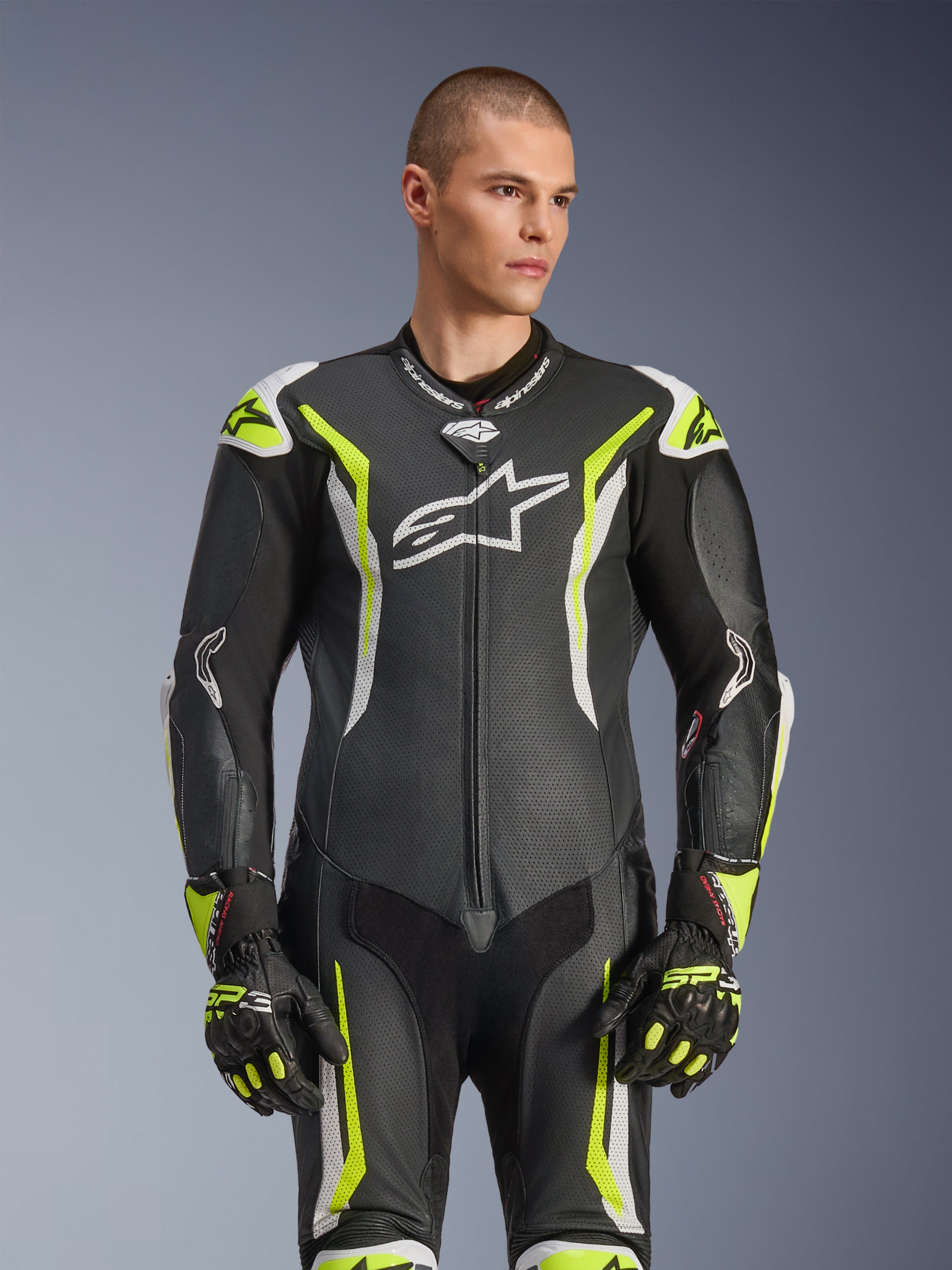 Alpinestars GP Tech V5 Einteiliger Lederkombi, Schwarz, Weiß und Gelb Fluo, professionelle Rennausrüstung, perforiertes Leder mit großem weißem Astar-Logo auf der Brust, neongelbe und weiße Akzente, getragen mit passenden Rennhandschuhen