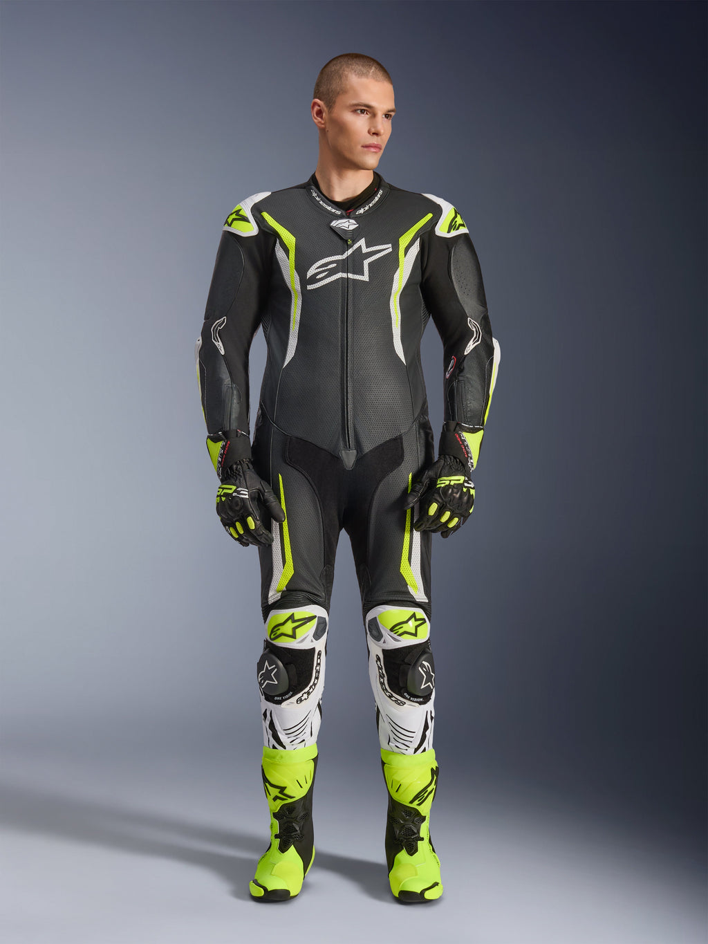 Alpinestars GP Tech V5 einteiliger Lederkombi, professioneller Motorrad-Rennanzug in Schwarz und Neongelb Fluo mit weißen Akzenten, getragen von einem Modell mit passenden Rennhandschuhen und Stiefeln, mit aerodynamischem Design und Schutz-Slidern.