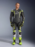 Alpinestars GP Tech V5 einteiliger Lederkombi, professioneller Motorrad-Rennanzug in Schwarz und Neongelb Fluo mit weißen Akzenten, getragen von einem Modell mit passenden Rennhandschuhen und Stiefeln, mit aerodynamischem Design und Schutz-Slidern.