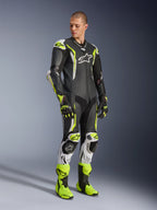 Alpinestars GP Tech V5 Einteiliger Lederkombi, Schwarz, Weiß und Gelb Fluo, getragen von einem Model mit passenden Rennhandschuhen und Stiefeln, professionelle Motorrad-Rennausrüstung mit aerodynamischer Performance und Schutzausrüstung.