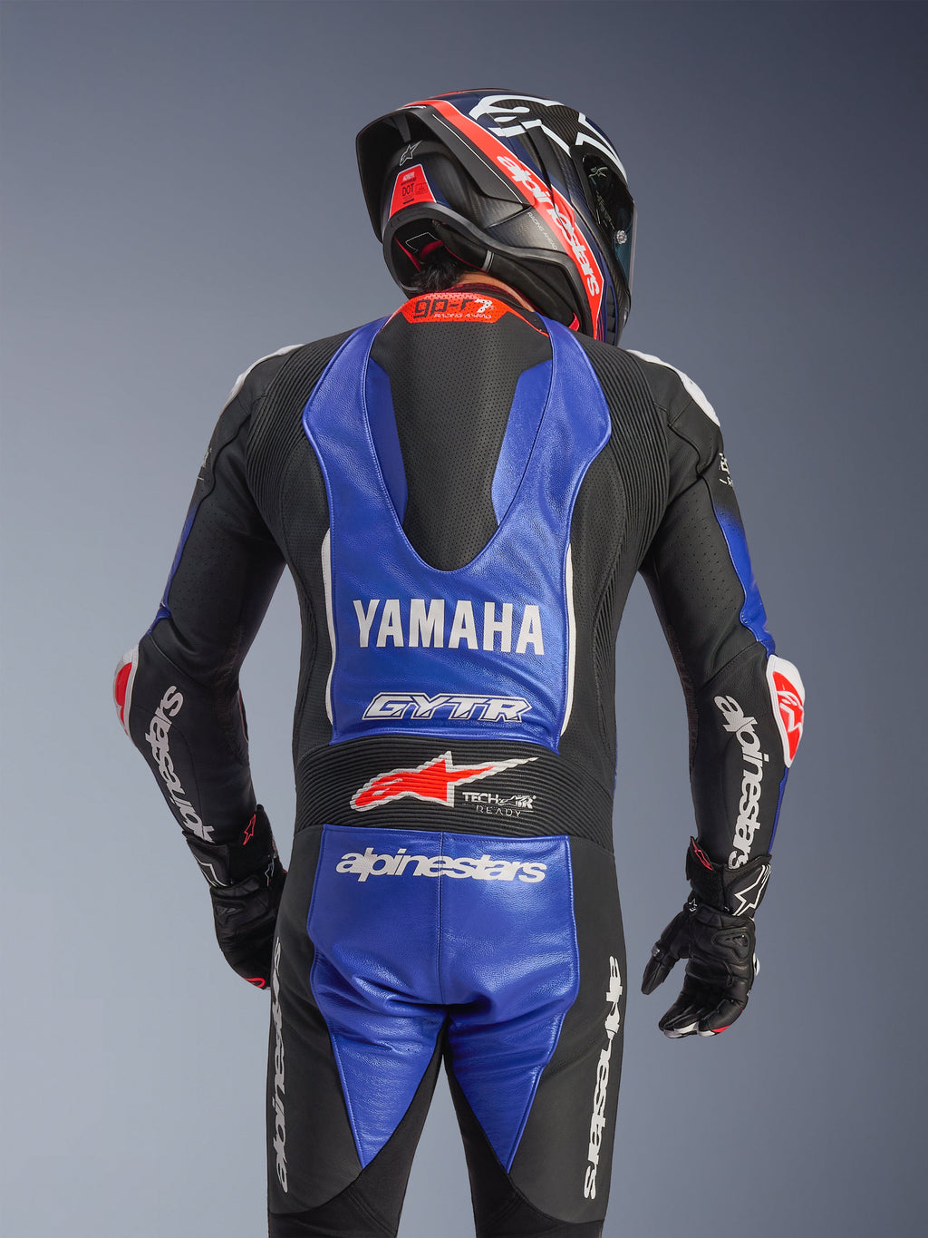 Alpinestars Yamaha GP-R7 One Piece Leather Suit, rear view, Metallic Blue and Black with white and red accents, prominent Yamaha and GYTR branding, featuring an aerodynamic speed hump, worn with a matching racing helmet and gloves for a professional track-ready look