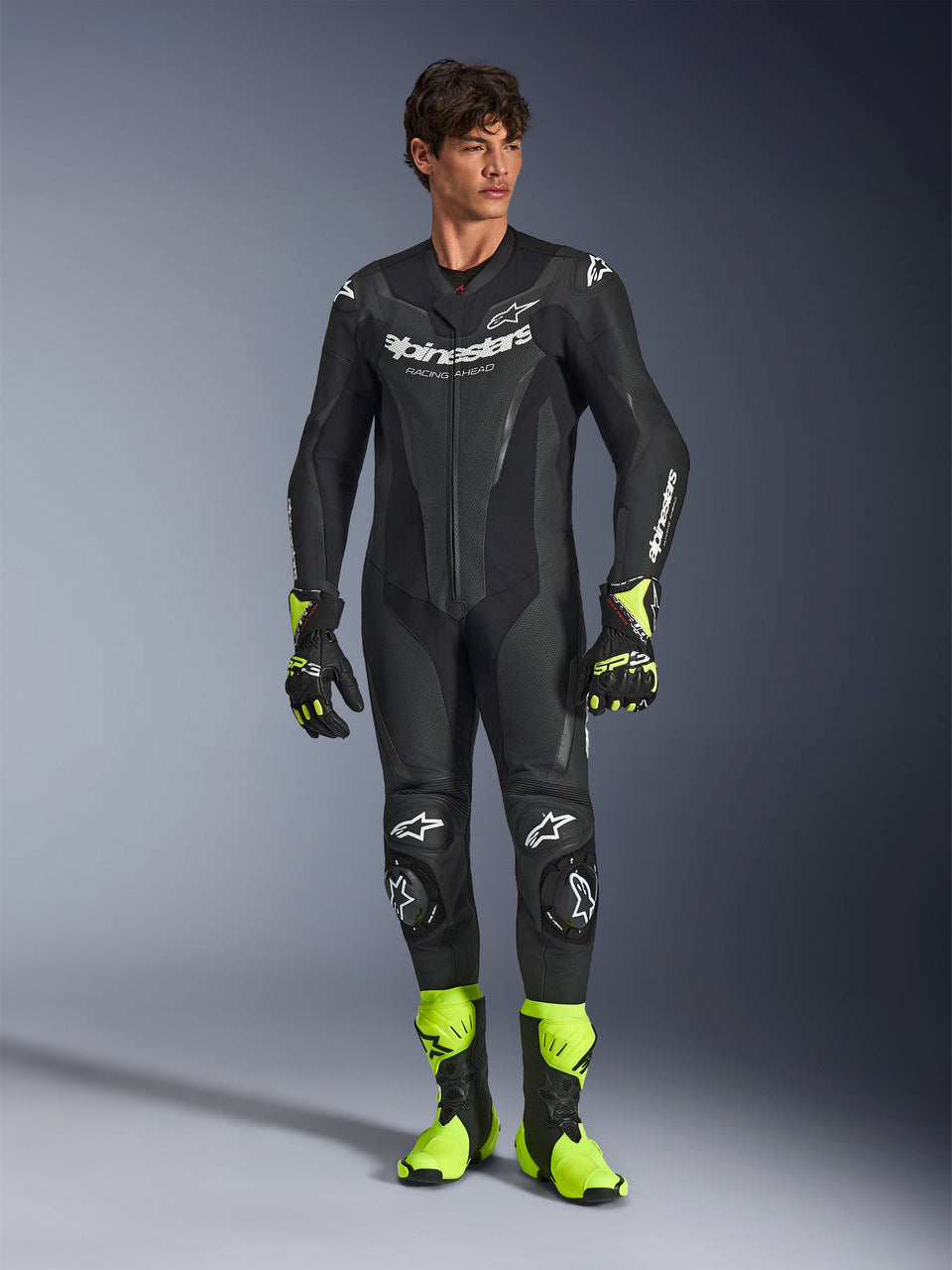 Alpinestars GP Force V2 Lederkombi, einteiliger schwarzer Motorradrennanzug, getragen mit neongelben Stiefeln und Handschuhen, mit weißen Logos und perforiertem Leder, schlankes Design für Trackdays