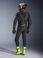 Rückansicht eines Fahrers im Alpinestars GP Force V2 1-teiligen Lederanzug in Schwarz, zeigt den aerodynamischen Speed-Hump und das Tech-Air Ready Branding, kombiniert mit einem schwarz-neongelben Helm und leuchtend gelben Rennstiefeln.