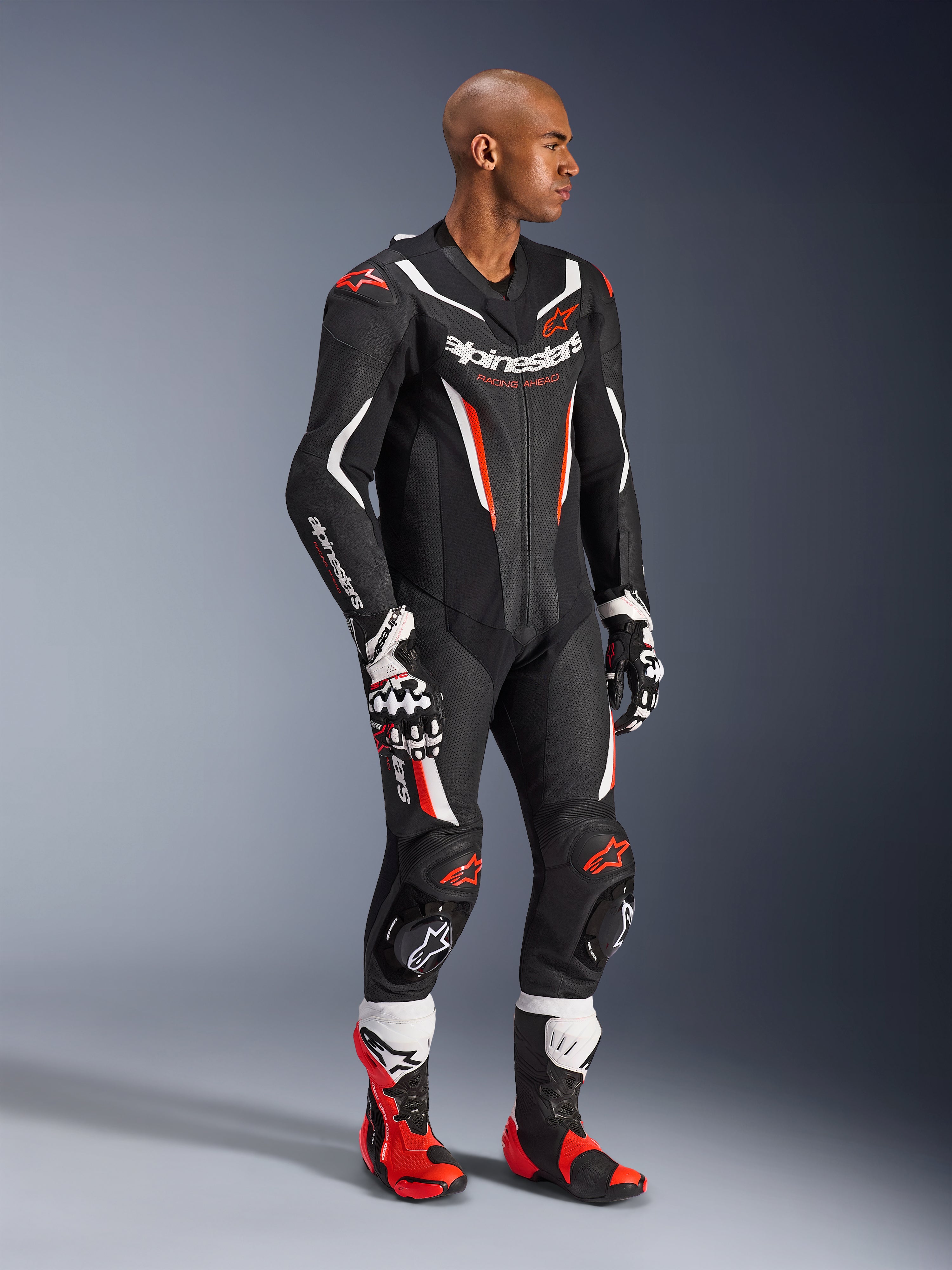 Alpinestars GP Force V2 Lederkombi – 1-teilig, Schwarz, Weiß und Fluo-Rot, getragen mit passenden Rennhandschuhen und Stiefeln, mit perforierten Ledereinsätzen, markanten weißen und roten Akzenten und Alpinestars-Branding auf der Brust und den Ärmeln, entwickelt für Performance auf der Rennstrecke.