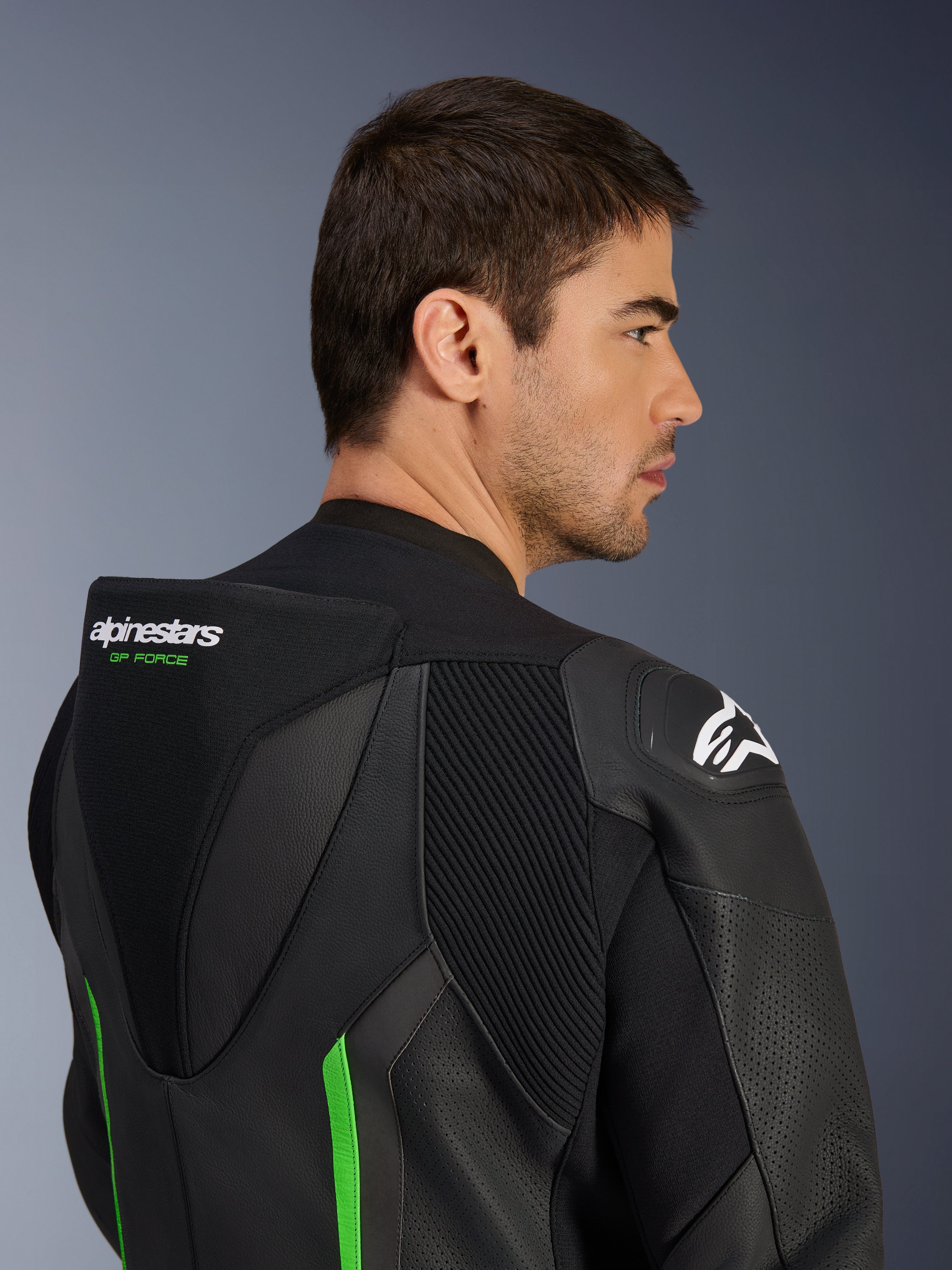 Nahaufnahme des oberen Rückens und der Schulter eines männlichen Models in der Alpinestars GP Force V2 Lederkombi in Schwarz-Grün, mit aerodynamischem Geschwindigkeitsbuckel mit grünem „GP FORCE“-Branding, weißem Astars-Logo auf der Schulter und Akkordeon-Stretch-Paneelen.
