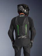 Rückansicht eines Fahrers im Alpinestars GP Force V2 Lederkombi in Schwarz-Grün, mit aerodynamischem Höcker, Tech-Air Ready-Branding auf dem Akkordeon-Einsatz am unteren Rücken und perforierter Lederkonstruktion, kombiniert mit einem schwarzen Carbon-Rennhelm.