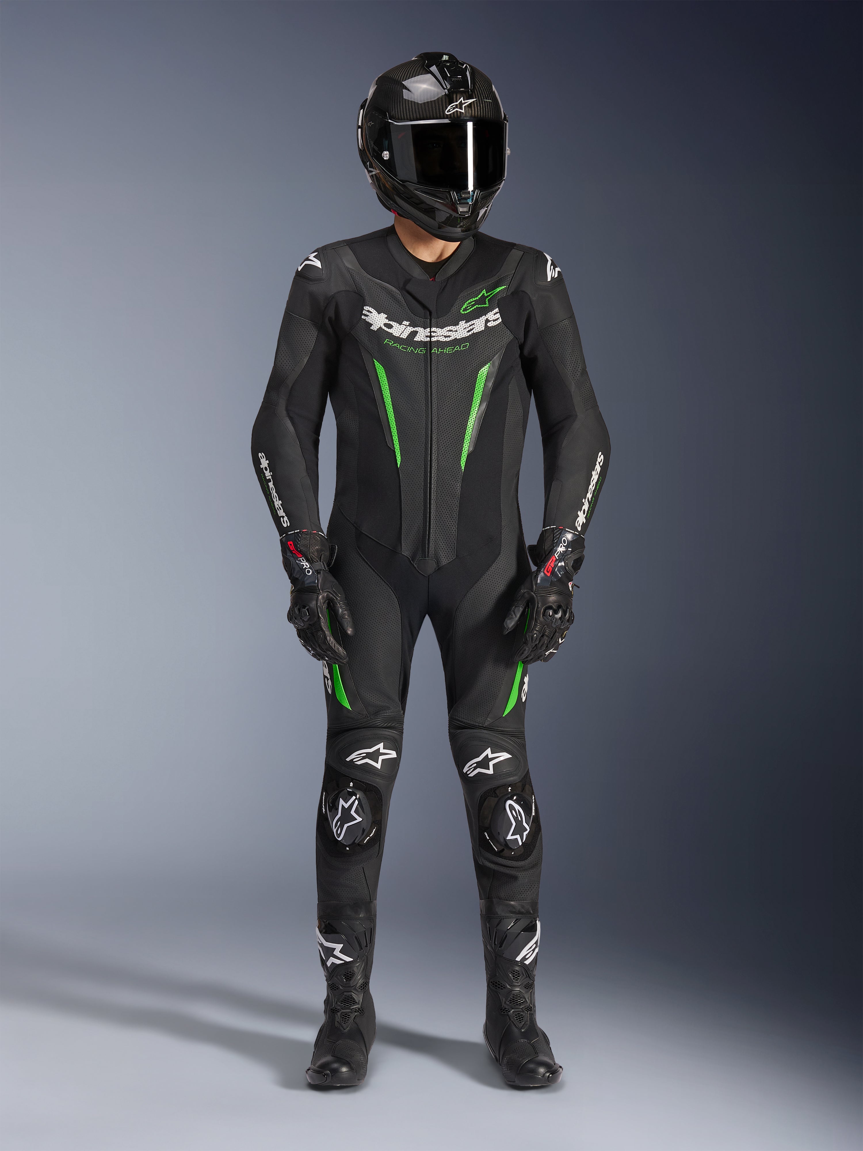 Motorradrennfahrer in Alpinestars GP Force V2 Lederkombi - 1-Teiler in Schwarz und Grün, kombiniert mit Carbon-Helm und Rennhandschuhen, mit perforierten Lederpaneelen und weißen Alpinestars-Logos, professionelle Ausrüstung für Rennstrecke und sportliches Fahren