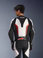 Alpinestars GP Force V2 Lederkombi 1-teilig, Weiß, Schwarz und Rot Fluo, Rückansicht an einem männlichen Model, mit aerodynamischem Höcker, perforierten Lederbahnen und Tech-Air Ready-Logo am unteren Rücken, professionelle Rennausrüstung mit schwarz-weißen Handschuhen