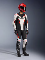 Alpinestars GP Force V2 Lederkombi 1-teilig in Weiß Schwarz und Rot Fluo, Ganzkörper-Studioaufnahme eines Fahrers in kompletter Rennausrüstung mit rotem Helm, schwarzen Handschuhen und schwarzen Stiefeln, aerodynamische Rindslederkonstruktion mit markantem Branding und integrierten Knieschleifern.