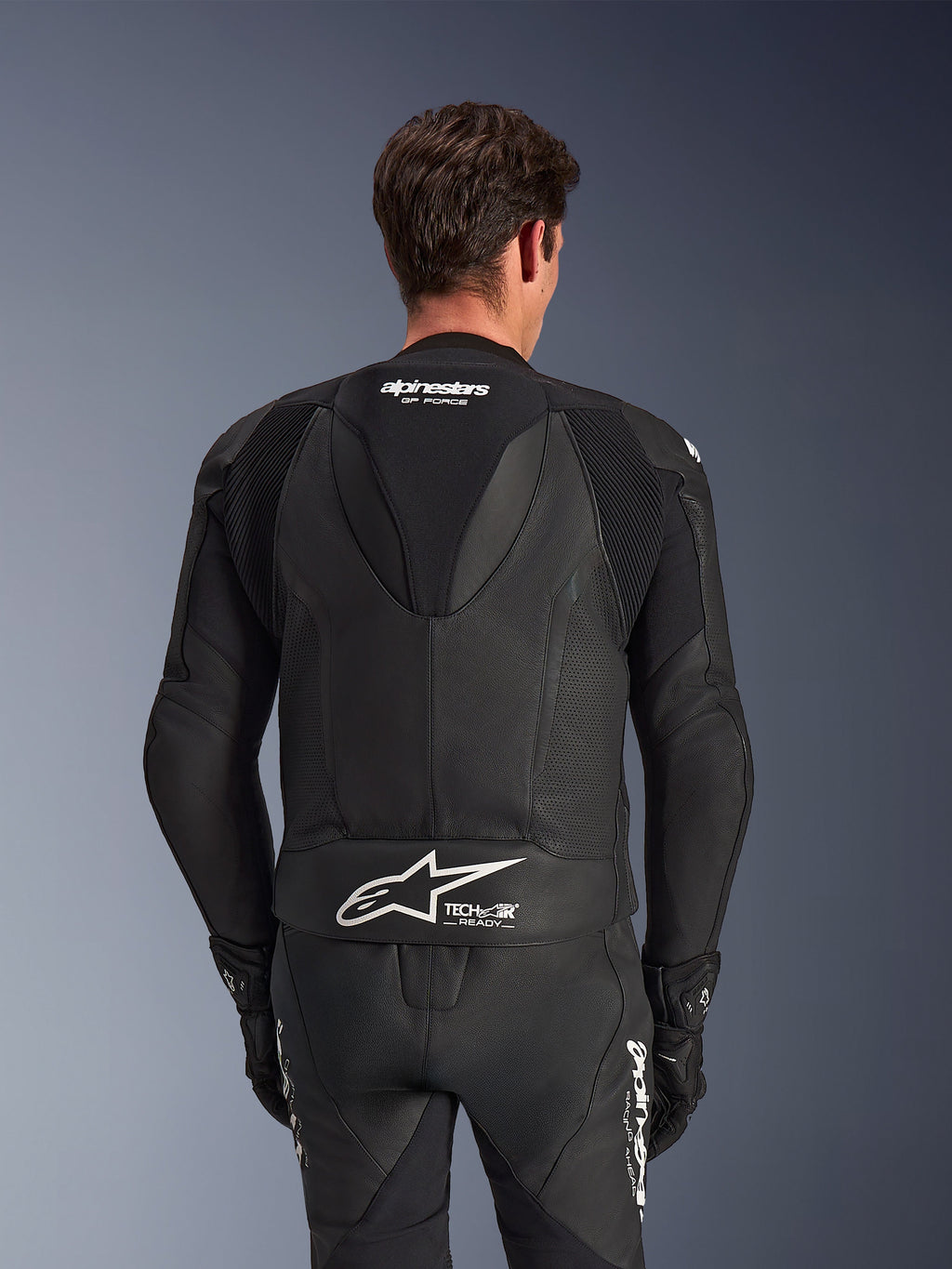 Alpinestars GP Force V2 Leather Suit- 2Piece, Black, back view of rider, featuring perforated leather panels, aerodynamic speed hump with GP Force branding, and white Alpinestars logo with Tech-Air Ready text on the lower back.