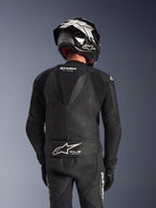 Alpinestars GP Force V2 2-Piece Leather Suit, black, back view of rider showing aerodynamic speed hump, perforated leather panels, and accordion stretch zones on shoulders, with Tech-Air Ready branding on the lower back, worn with matching racing helmet and gloves.