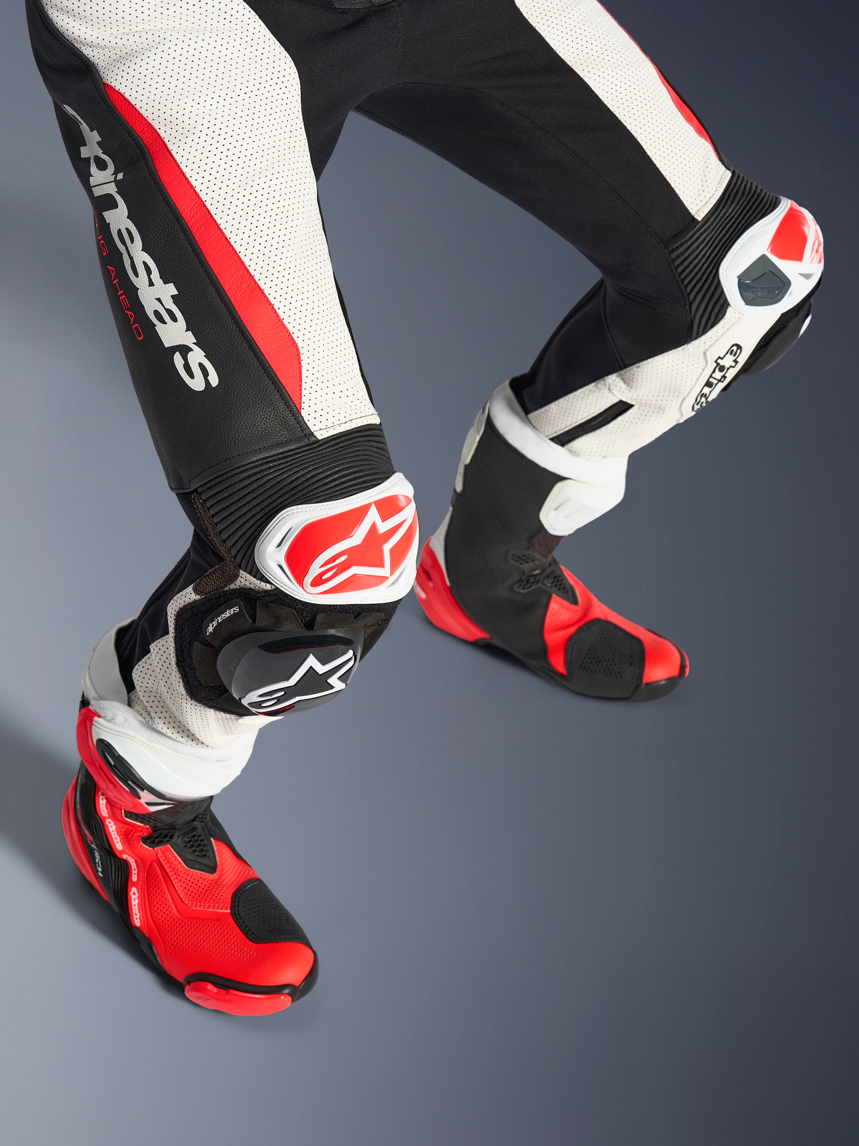 Alpinestars Damen Stella GP-R7 2-Teiler Lederkombi, Unterschenkel und Rennstiefel, Schwarz, Weiß und Rot Fluo, mit perforiertem Leder, markantem Alpinestars-Logo am Oberschenkel, Akkordeon-Stretch-Einsätzen, rot-weißen Knieschleifern und passenden rot-schwarzen technischen Stiefeln.