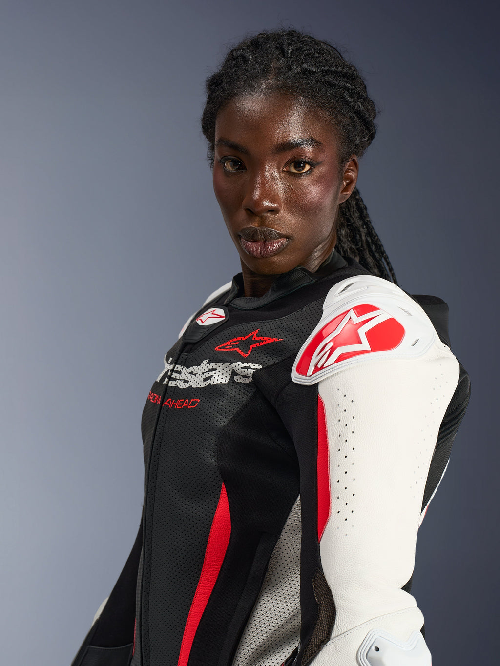 Motorradfahrerin im Alpinestars Stella GP-R7 2-Teiler-Lederanzug, Schwarz, Weiß und Rot Fluo, mit weißen Schulterprotektoren und rotem Stern-Logo, perforiertem Lederbrustbereich und professionellem, vom Rennsport inspiriertem Design