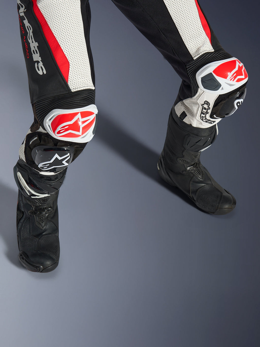 Alpinestars Stella GP-R7 2-Teiler-Lederanzug für Damen, Schwarz, Weiß und Rot Fluo, Nahaufnahme der Beine und Knie mit rot-weißen GP DFS RR Knieschleifern, perforierte Lederkonstruktion mit Akkordeon-Stretchpaneelen, getragen mit schwarzen Performance-Rennstiefeln