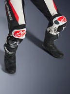 Alpinestars Stella GP-R7 2-Teiler-Lederanzug für Damen, Schwarz, Weiß und Rot Fluo, Nahaufnahme der Beine und Knie mit rot-weißen GP DFS RR Knieschleifern, perforierte Lederkonstruktion mit Akkordeon-Stretchpaneelen, getragen mit schwarzen Performance-Rennstiefeln
