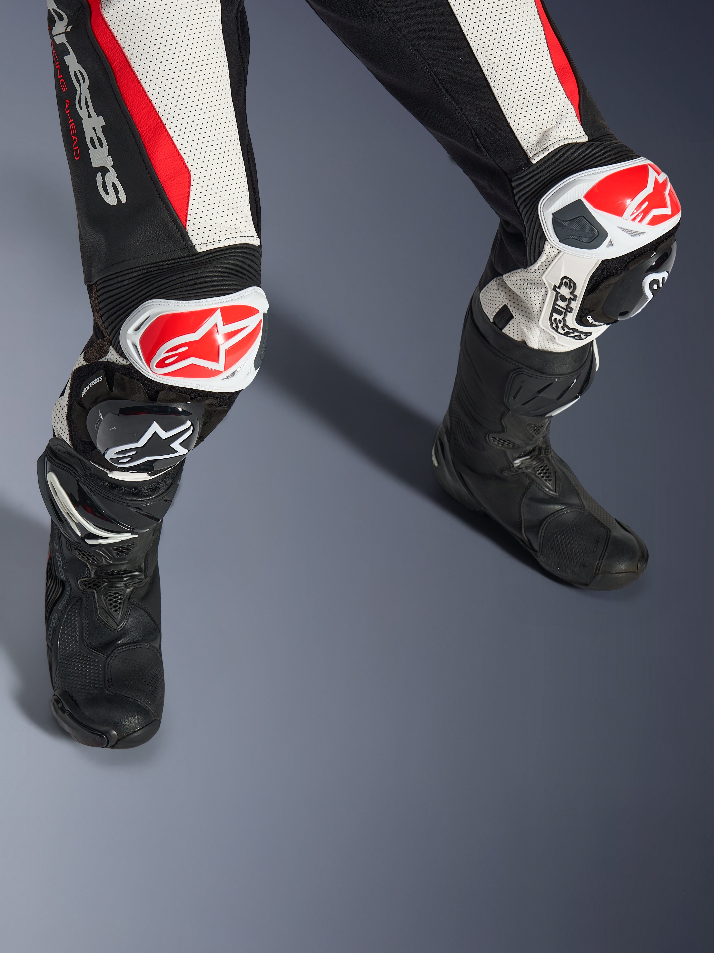 Alpinestars Stella GP-R7 2-Teiler-Lederanzug für Damen, Schwarz, Weiß und Rot Fluo, Nahaufnahme der Beine und Knie mit rot-weißen GP DFS RR Knieschleifern, perforierte Lederkonstruktion mit Akkordeon-Stretchpaneelen, getragen mit schwarzen Performance-Rennstiefeln