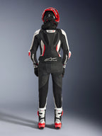 Alpinestars Stella GP-R7 2-Teiler-Lederanzug für Damen, Rückansicht, Schwarz, Weiß und Rot Fluo, mit aerodynamischem Höcker und GP-R7-Branding, Tech-Air Ready-Logo am unteren Rücken, Akkordeon-Stretch-Einsätzen und Alpinestars-Branding auf den Ärmeln, getragen mit passendem Helm und Stiefeln