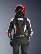 Alpinestars Stella GP-R7 2-Teiler-Lederanzug für Damen, Schwarz, Weiß und Fluo-Rot, Rückansicht einer Fahrerin mit rotem Helm und schwarzen Handschuhen, aerodynamischer Höcker mit GP-R7-Branding und Tech-Air Ready-Logo am unteren Rücken.