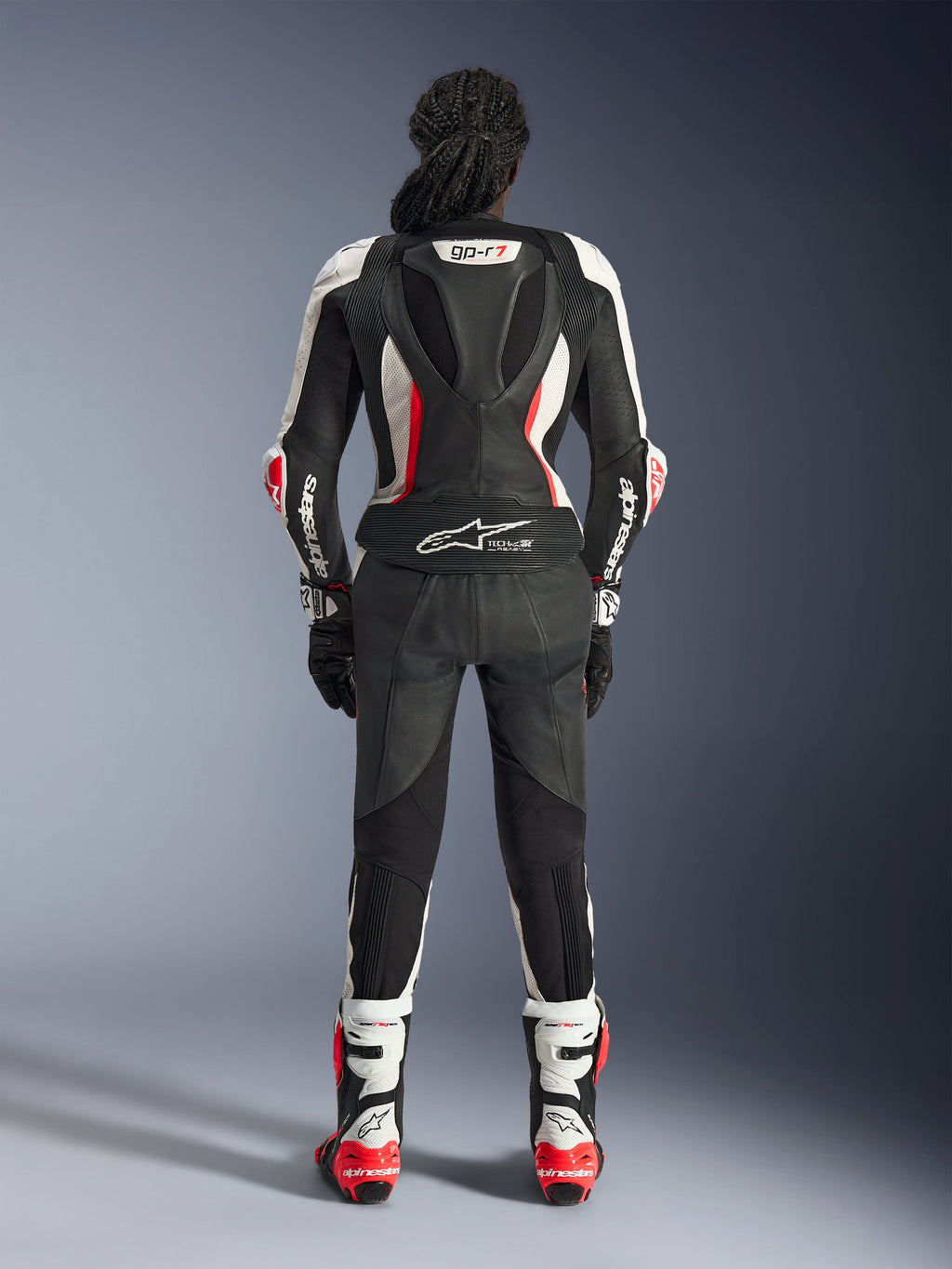 Rückansicht des Alpinestars Stella GP-R7 2-teiligen Lederanzugs, Schwarz, Weiß und Fluo-Rot, mit einem aerodynamischen Höcker samt GP-R7-Branding und Tech-Air Ready-Logo, getragen mit passenden Rennstiefeln und Handschuhen, professionelle Motorradausrüstung für Damen